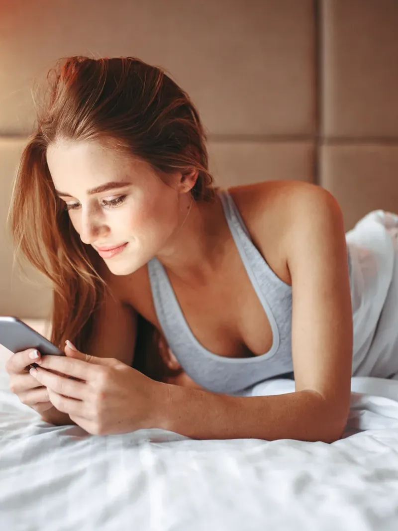 Hôtesse allongée sur son lit qui consulte son téléphone